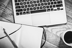 [ai] A top view of a laptop keyboard, a blank notebook with a pen, and a white coffee cup on a wooden table.